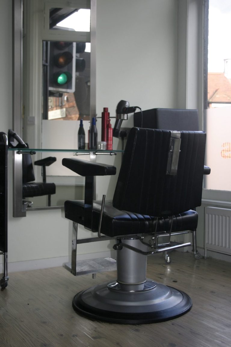 A Barber chair in front of a mirror with hair products on the counter.